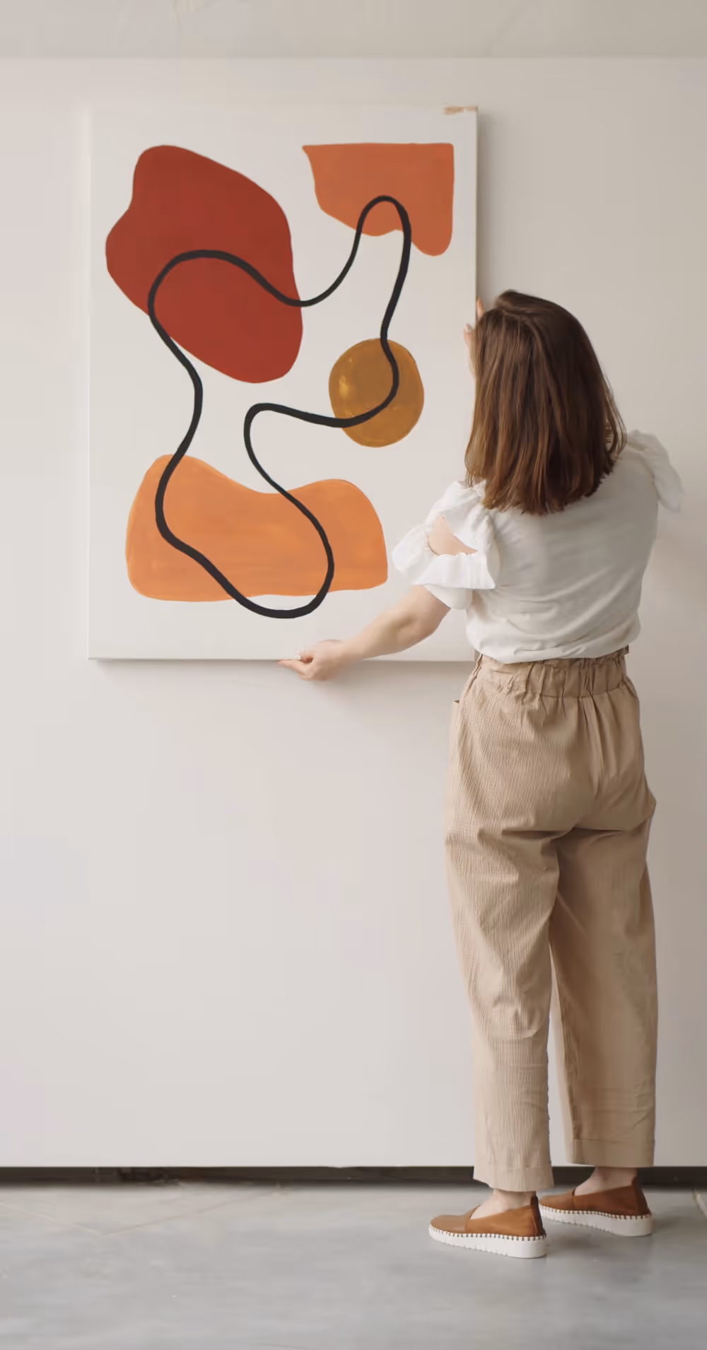 Woman hanging abstract painting with warm tones